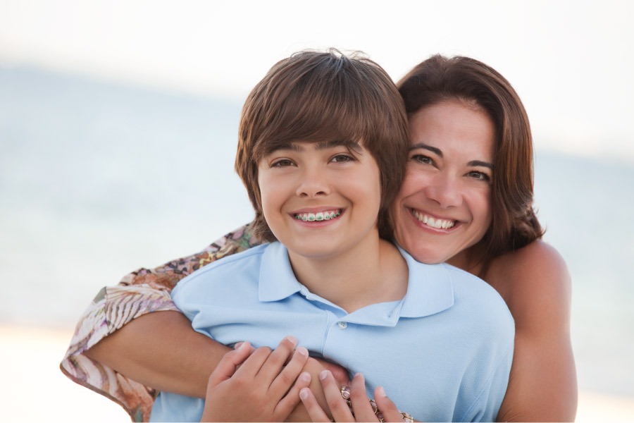Brunette mom smiles with her son in a blue polo after he gets his braces on