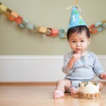 Asian baby celebrating his or her first birthday with a party hat, cake and paper chain.