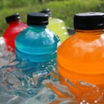 Closeup of orange, blue, red, and yellow sports drinks in a tub of ice water outside