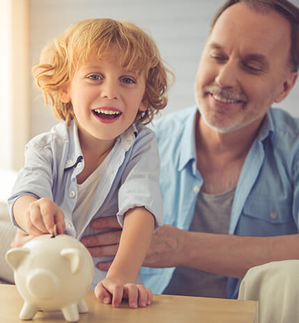 little boy putting a coin in a piggy bank while his grandfather holds him